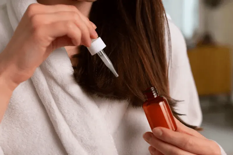 The image shows a woman applying a hair serum with a dropper, highlighting the use of professional hair care solutions to maintain and enhance hair health.