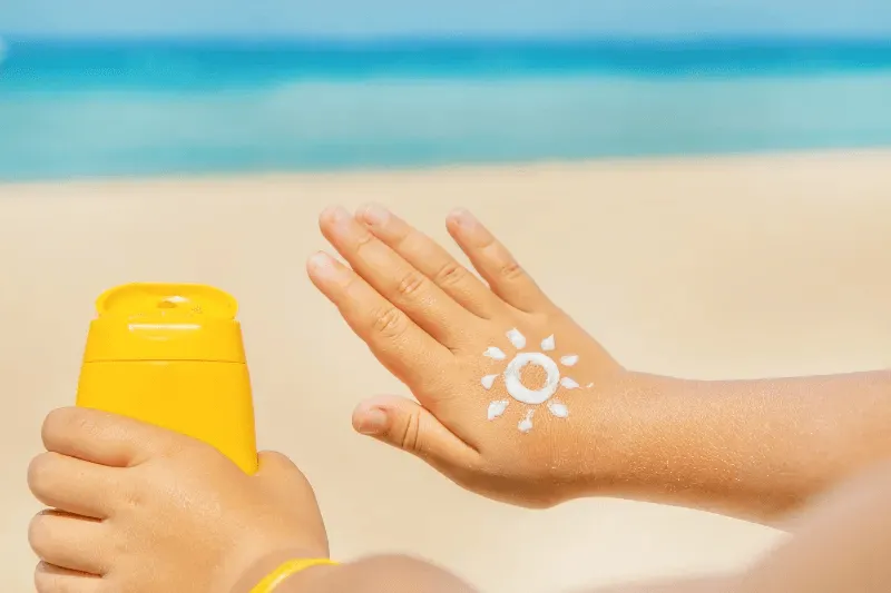 This image shows a hand applying sunscreen with a sun symbol drawn on the skin, symbolizing the importance of sun protection.