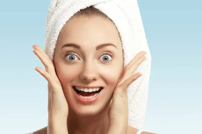 The image portrays a cheerful woman with a towel wrapped around her head, highlighting her glowing, fresh skin.